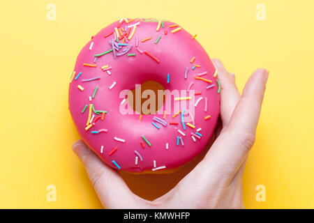 Woman's hand takes a strawberry donut in the glaze on a bright orange background. Stock Photo