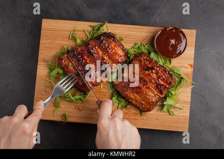 Hands of young woman cutting delicious pork ribs bbq in kitchen. Top view. Stock Photo