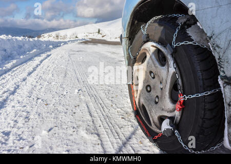 Closeup of snow chains mounted on a snowy car wheel with large copy space on the left. Stock Photo