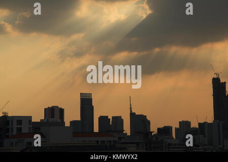 silhouette cityscape with powerful sun light beaming through dark cloudy sky. Stock Photo