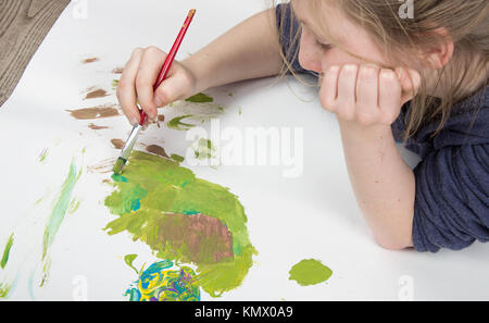 young child playing with paint brush in splattered paint on a white background Stock Photo