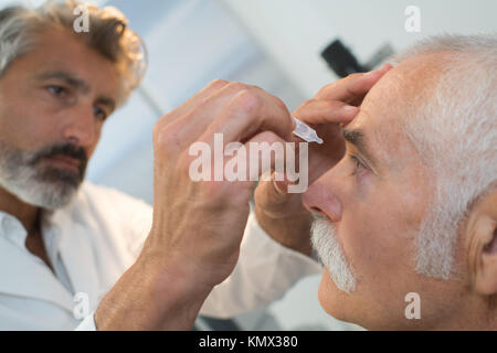 doctor putting eye drops in senior mans eyes Stock Photo