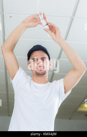 handsome young builder installing light bulb indoors Stock Photo