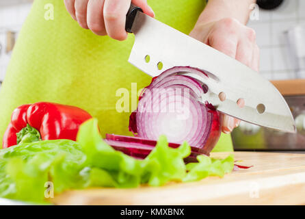 Woman's hands cutting bulb onion, behind fresh vegetables. Stock Photo