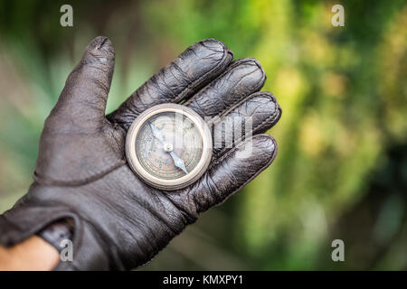 Man's hand in a leather glove holding a compass. Nature background. Stock Photo