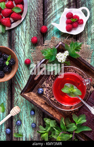 Herbal tea from strawberry, blueberry, raspberry, blackberry and mint leaves on green rustic background in summer time Stock Photo