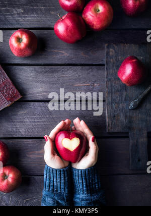 Woman holding red apple with carved heart on dark wooden background Stock Photo
