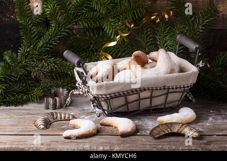 Homemade sugar cookies crescent served in basket with vintage cookie-cutters near christmas tree over old wooden table Stock Photo