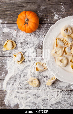 Top view on plate of homemade pasta ravioli over wooden table with flour and orange pumpkin Stock Photo