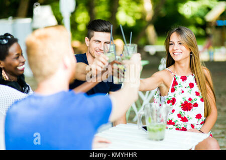 Group of cheerful happy people toasting while sitting at a table Stock Photo