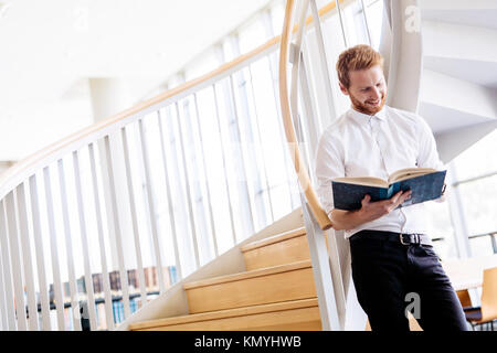 Handsome intelligent guy reading a book in a library Stock Photo
