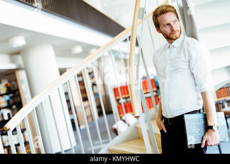 Handsome intelligent guy reading a book in a library Stock Photo