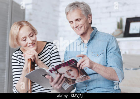 Positive minded elderly married couple reading magazine Stock Photo