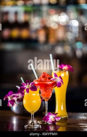 Composition with 3 yellow and red cocktails and orchid flowers on the blurred background Stock Photo