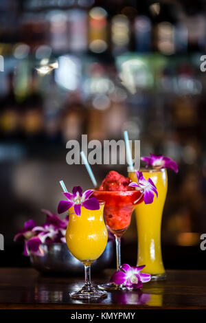 Composition with 3 yellow and red cocktails and orchid flowers on the blurred background Stock Photo