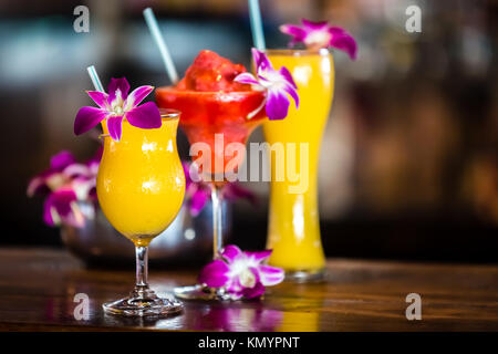 Composition with 3 yellow and red cocktails and orchid flowers on the blurred background Stock Photo