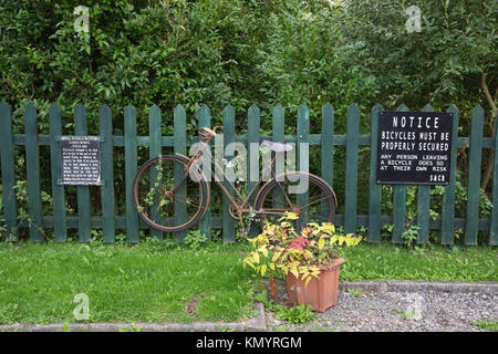 An old fashioned rusty Royal Enfield ladies bicycle with a bent pedal securely chained to the wooden fence at Blunsdon Railway station Stock Photo