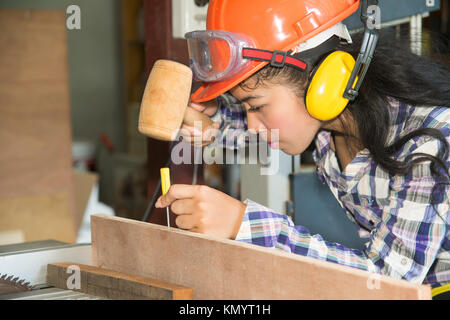 Asian pretty female carpenter using wood hammer for wood. Stock Photo