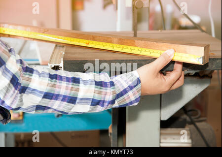 Pretty Asian woman carpenter is measuring wood  length with tape for cut by electric sander. Stock Photo