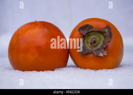Two ripe orange persimmons lie in the snow on the table Stock Photo