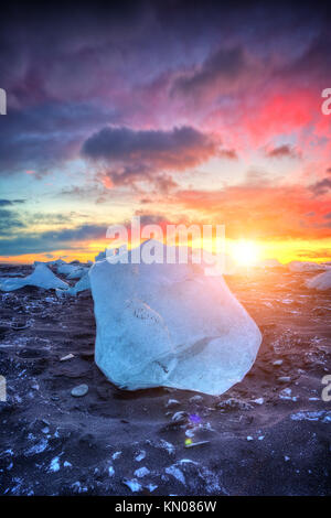 Beautiful sunset over famous Diamond beach, Iceland. This sand lava beach is full of many giant ice gems, placed near glacier lagoon Jokulsarlon. Stock Photo