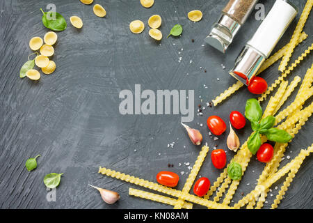 Italian foods concept and menu design. Mix of pasta, cheese, spices, tomatoes and basil on a gray slate background. Flat lay, top view with copy space Stock Photo