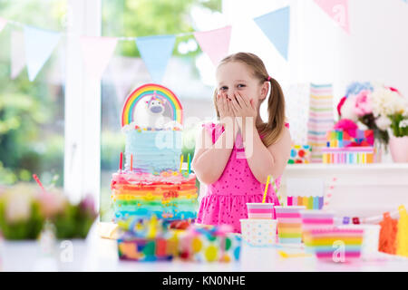 Kids birthday party with colorful pastel decoration and unicorn rainbow cake. Little girl with sweets, candy and fruit. Balloons and banner at festive Stock Photo