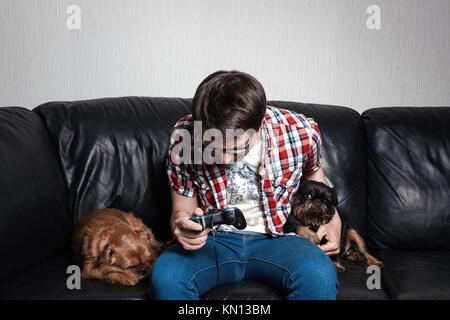 A young man in a red shirt and blue jeans sits at home and plays video games together with their dogs. Poor guy is crying and angry because of fail. t Stock Photo
