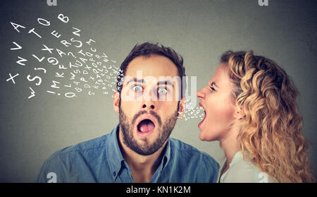 Angry woman screaming something in the ear of a shocked, scared guy isolated on gray wall background. Stock Photo