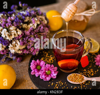 dripping honey from wooden dipper on hot cup of tea Stock Photo