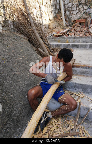Mexican man scraping bark fron tree limbs to make stair railings ...