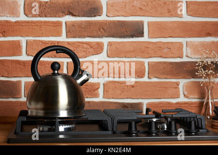 Close up of metal kettle on clean stove with red brick background Stock Photo