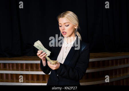 Beautiful blonde businesswoman with money at loft office in black suit. Stock Photo