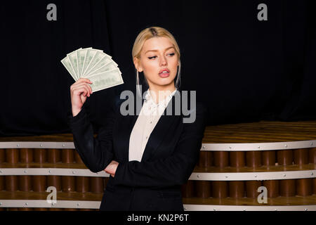 Beautiful blonde businesswoman with money at loft office in black suit. Stock Photo