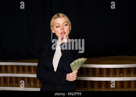 Beautiful blonde businesswoman with money at loft office in black suit. Stock Photo