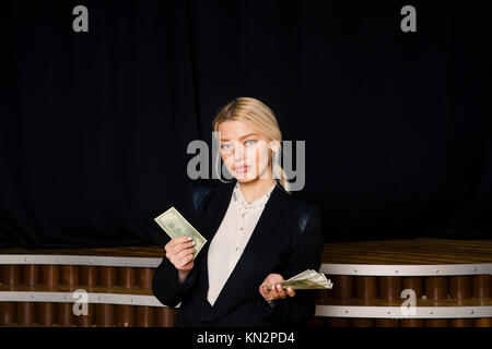 Beautiful blonde businesswoman with money at loft office in black suit. Stock Photo