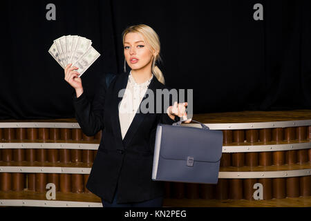 Beautiful blonde businesswoman with money at loft office in black suit. Stock Photo