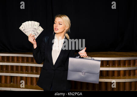 Beautiful blonde businesswoman with money at loft office in black suit. Stock Photo