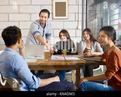 team of young asian and caucasian entrepreneurs meeting in office discussing business plan in office. Stock Photo