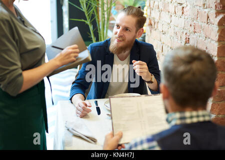 Portrait of handsome bearded man talking to waitress ordering food in modern cafe during business lunch time Stock Photo