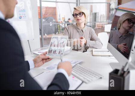 Portrait of successful blonde businesswoman discussing statistics report with colleague looking at graphs and charts with financial data during meetin Stock Photo