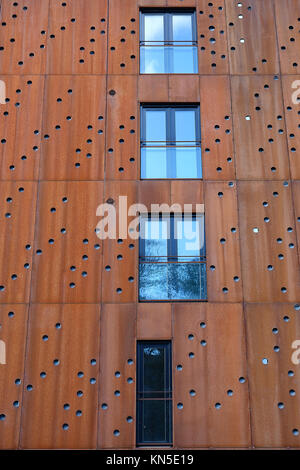 Windows with french balcony in building facade with rusty metal plates with round holes Stock Photo