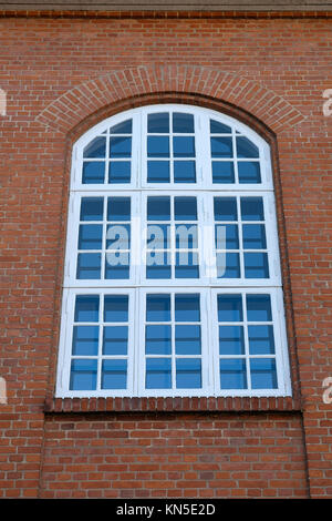 Big tall old white painted wood window with an arched top in a red brick facade Stock Photo