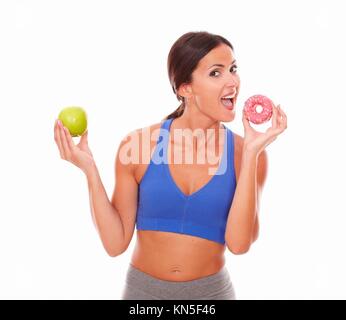 Lady wearing sports outfit biting sugary cake against white background.