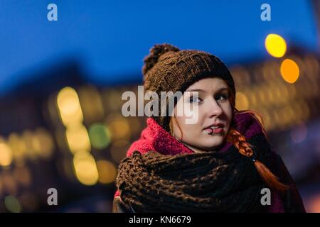 Attractive city woman wearing woolly hat, lights of city on background, focus on foreground.