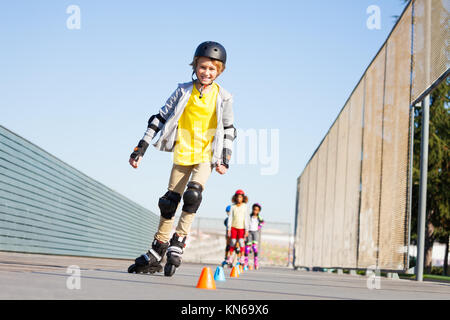 Portrait of preteen boy, happy inline skater, curving around the cones at slalom course in summer Stock Photo
