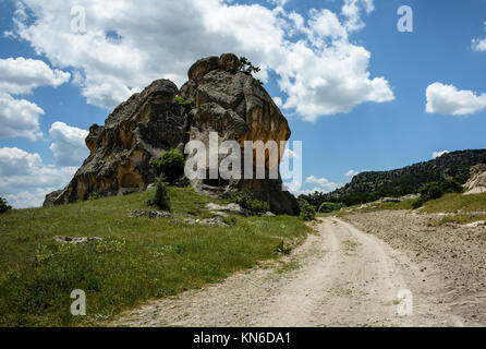 Beautiful landscape with a winding dirt road under blue skies with fluffy white clouds and historical rock formations Stock Photo