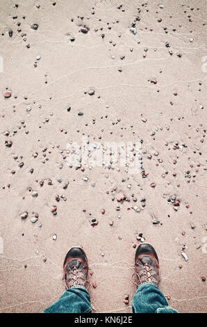 Person in hiking shoes stands on a beach, seen from above, color toned picture. Stock Photo