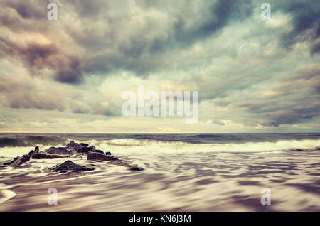 Vintage toned picture of a beach with stormy sky, motion blurred water. Stock Photo