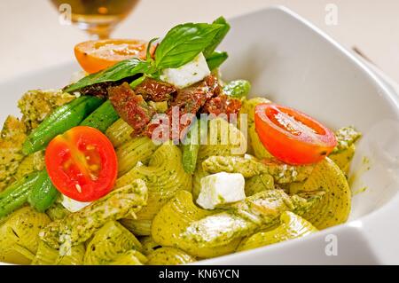 fresh lumaconi pasta and pesto sauce with vegetables and sundried tomatoes,tipycal italian food.